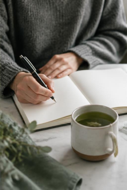 Hands recording notes in a journal beside a cup of tea